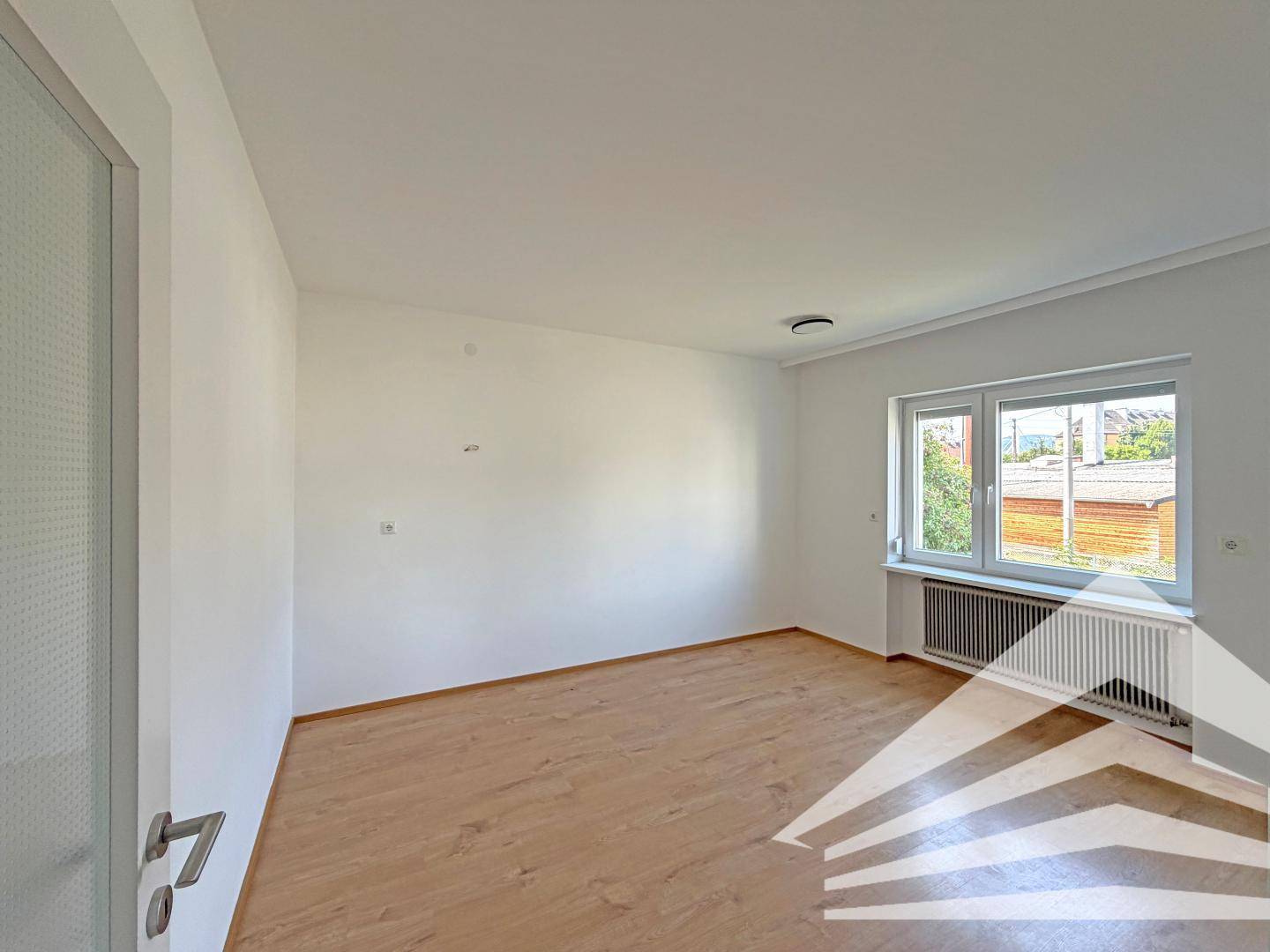 Geräumiges, helles Schlafzimmer mit Laminatboden und einem Fenster, das viel Tageslicht hereinlässt.
