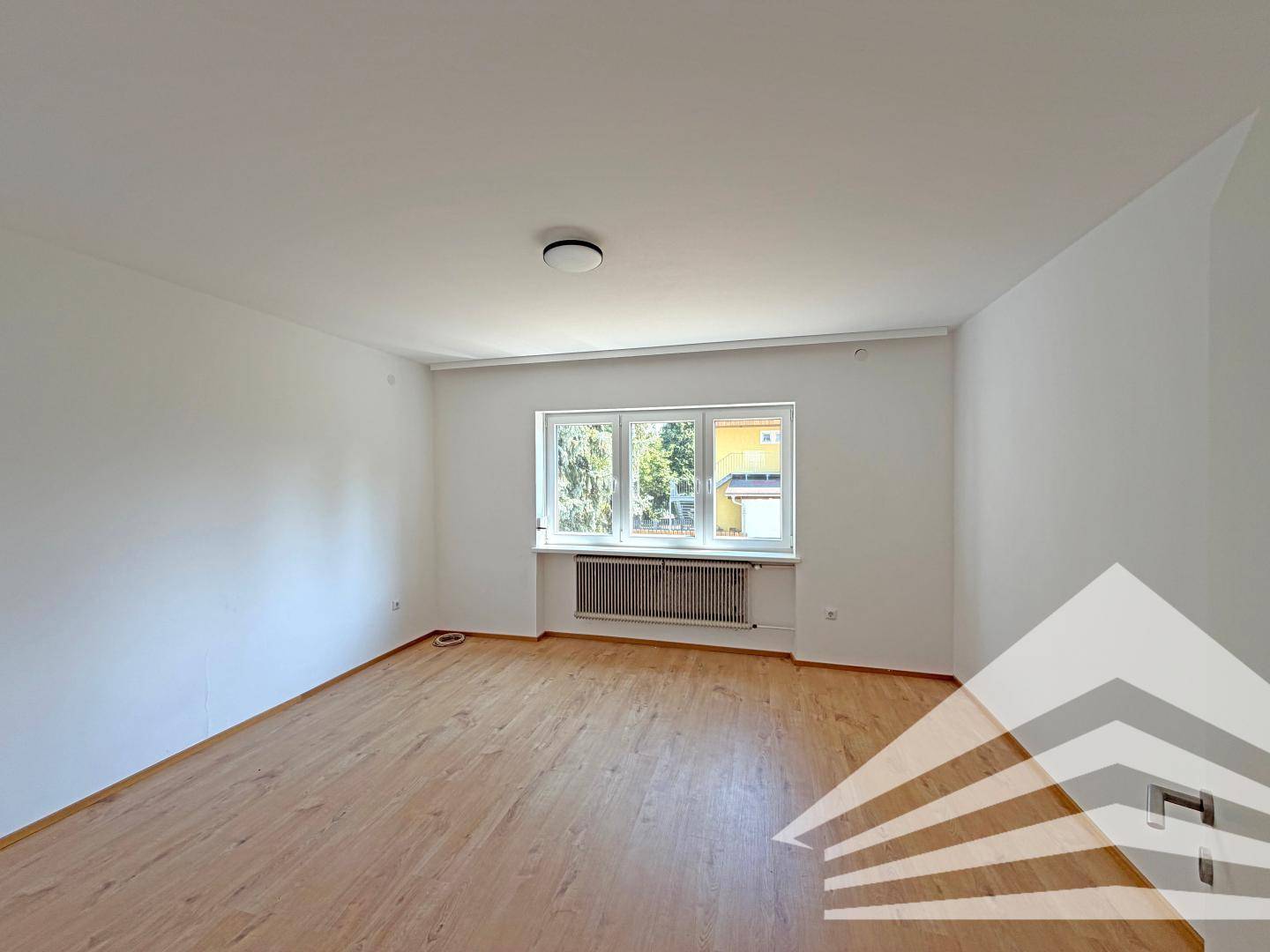 Geräumiges, helles Schlafzimmer mit Laminatboden und einem großen Fenster mit Blick ins Grüne.