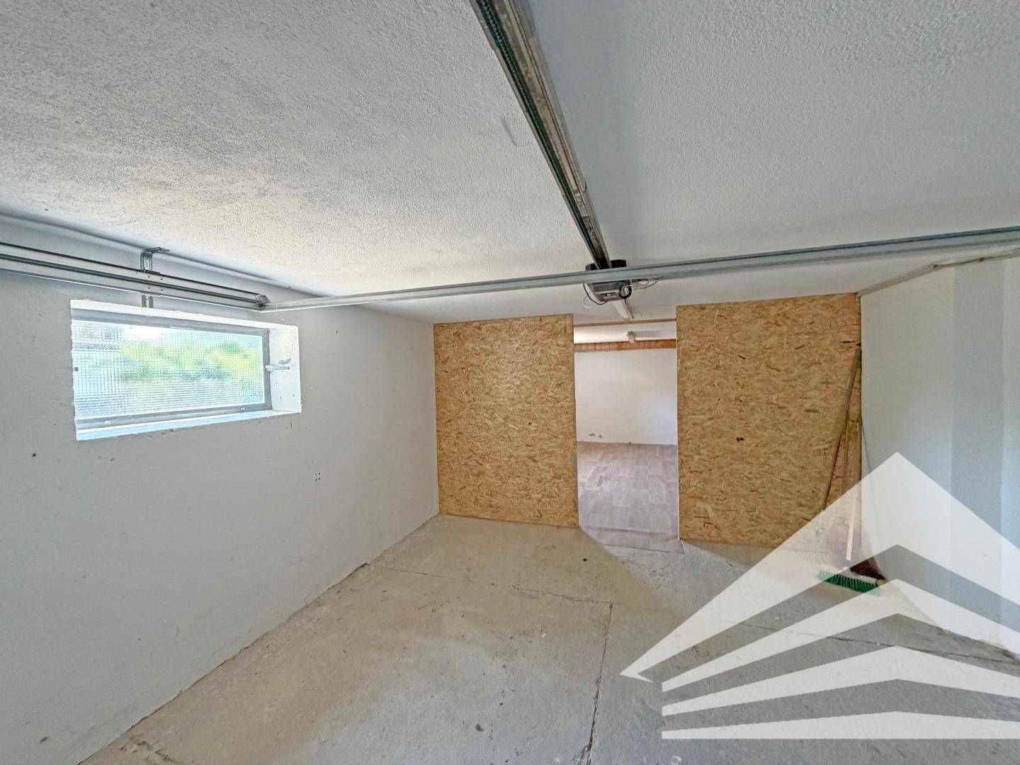 Innenansicht der Garage mit Betonboden und Zugang zu einem weiteren Raum im hinteren Bereich.