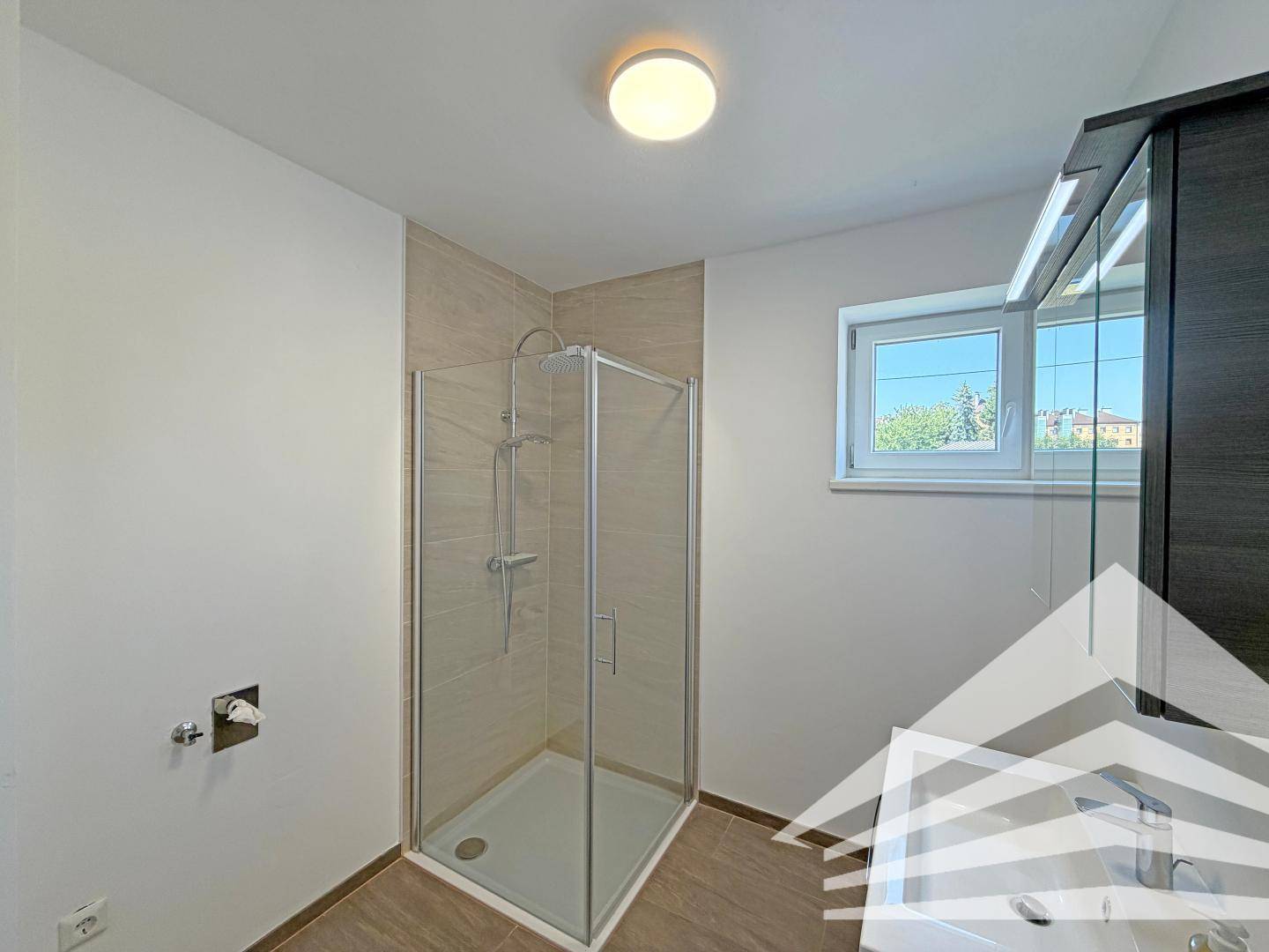 Modernes Badezimmer mit Duschkabine, Fliesenboden und einem Fenster für natürliche Belüftung.