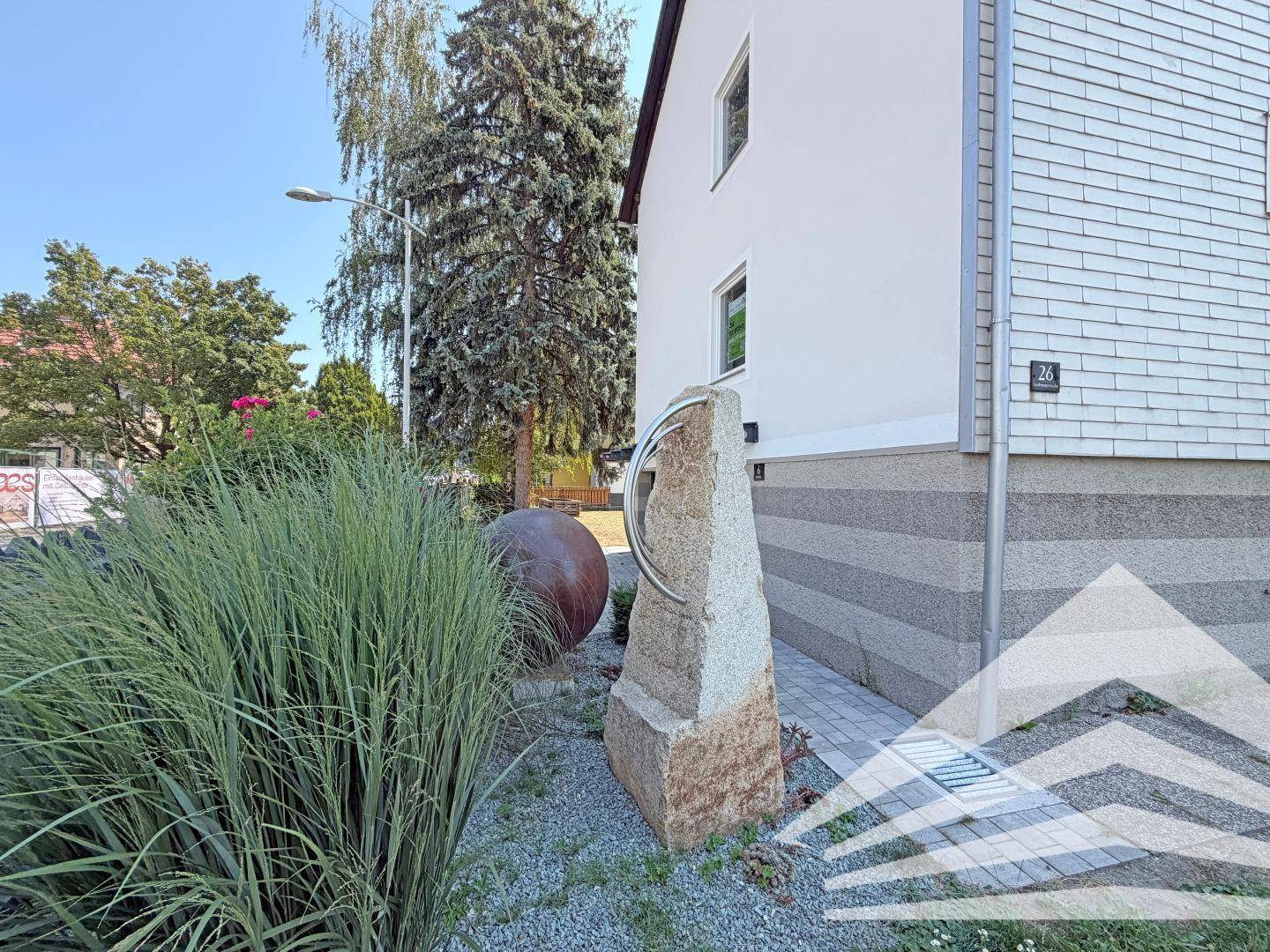 Seitenansicht des Hauses mit dekorativen Steinelementen und Pflanzen im Vorgartenbereich.