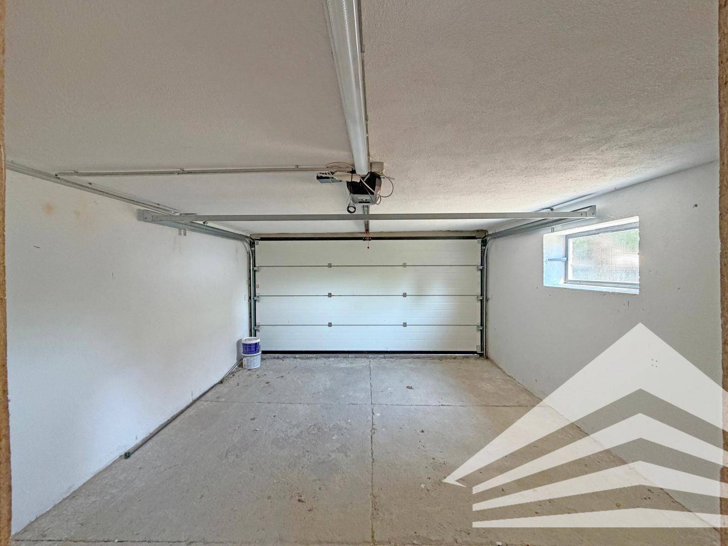 Geräumige Garage mit automatischem Tor, Betonboden und einem kleinen Fenster für Belüftung.