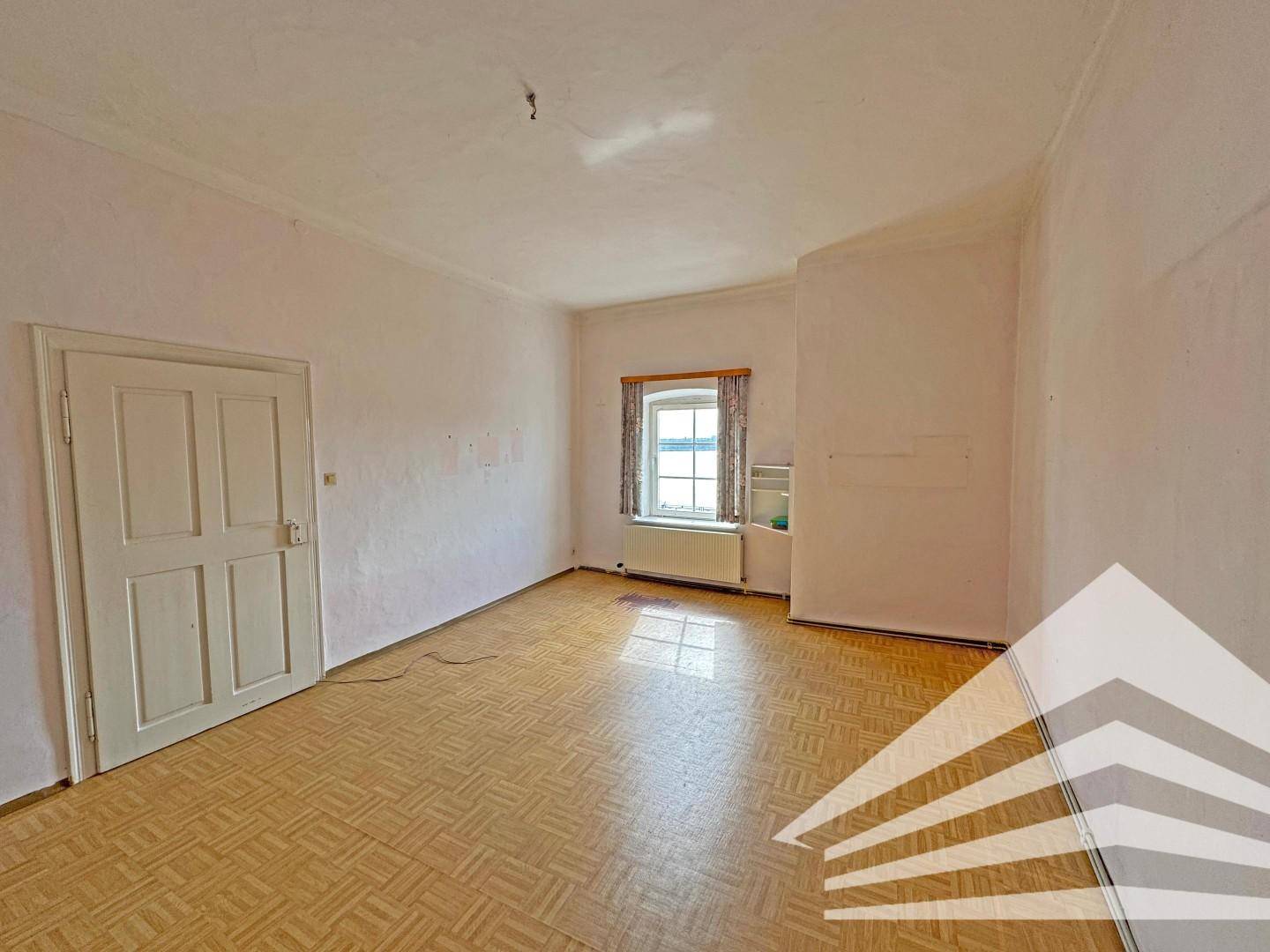 Helles Zimmer mit Laminatboden, einem Fenster und einer weißen Tür.