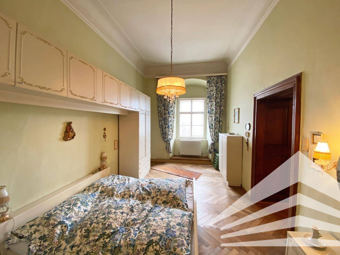 Schlafzimmer mit Parkettboden, Einbauschränken und einem Fenster mit Vorhängen.