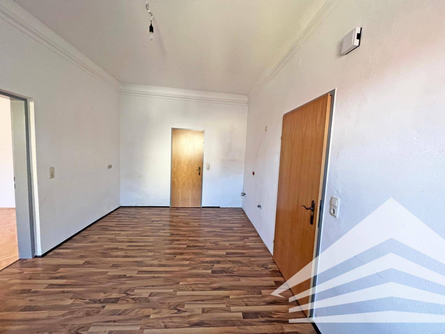 Geräumiges Zimmer mit Laminatboden in Holzoptik und weißen Wänden.