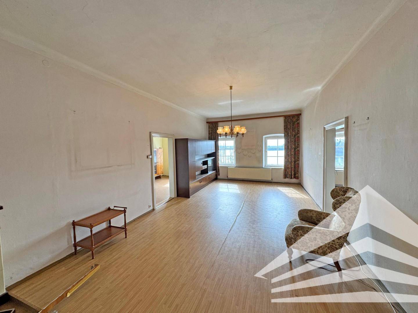 Geräumiges Wohnzimmer mit Laminatboden, hohen Decken und einem großen Fenster.