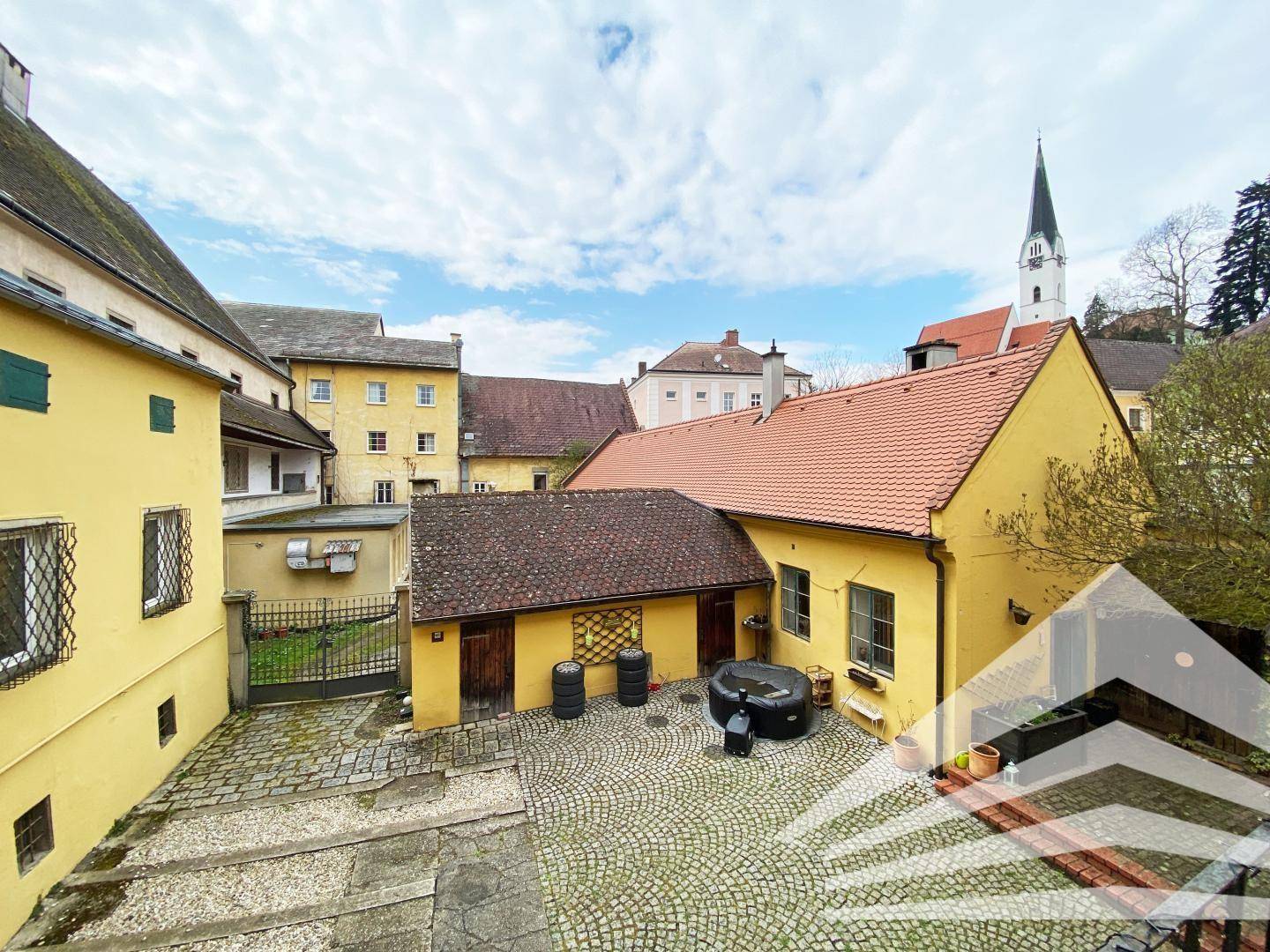 Gepflasterter Innenhof mit Whirlpool und Nebengebäuden, im Hintergrund eine Kirche.