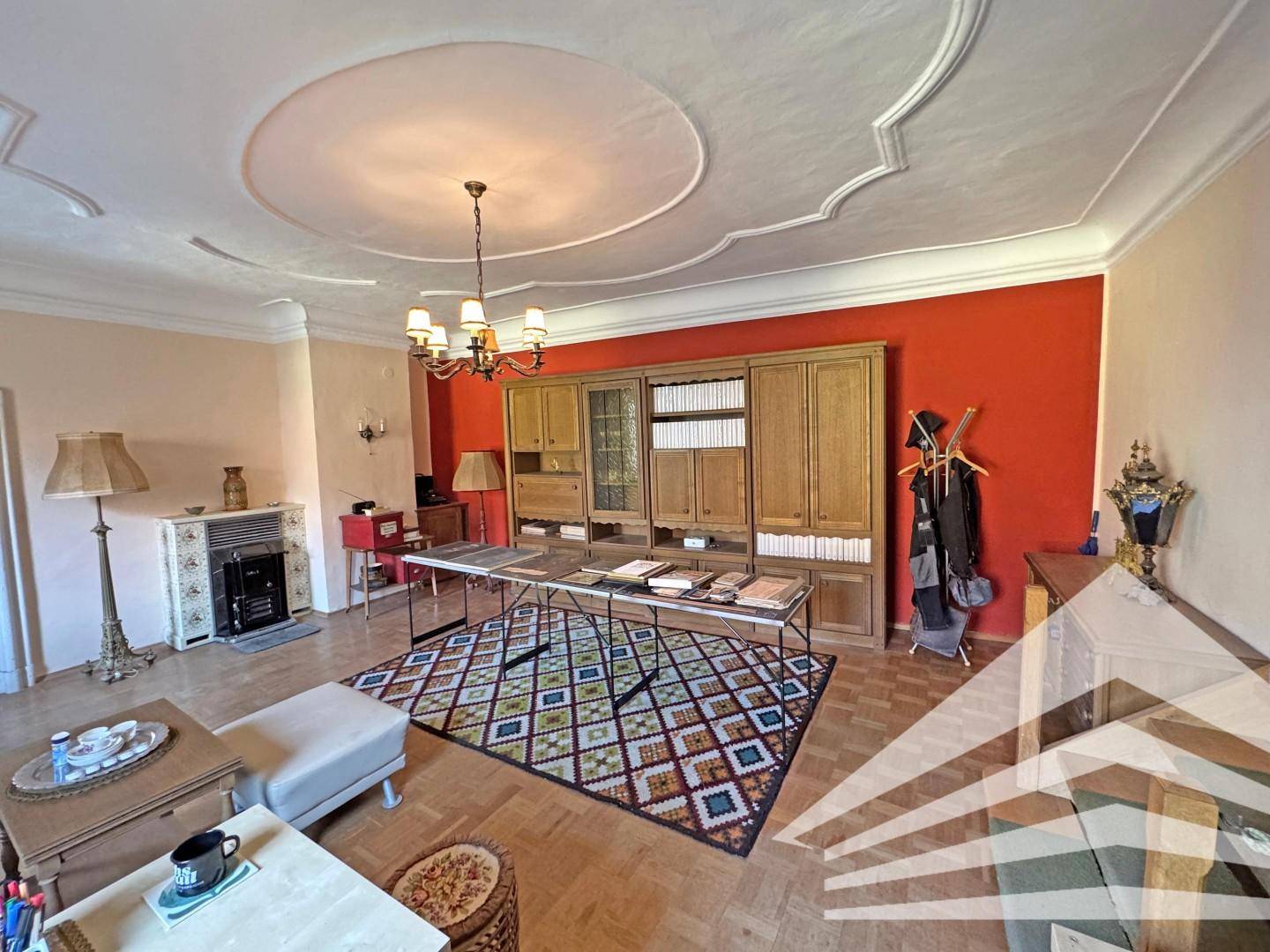 Geräumiges Wohnzimmer mit Parkettboden, Kamin und einer roten Akzentwand.