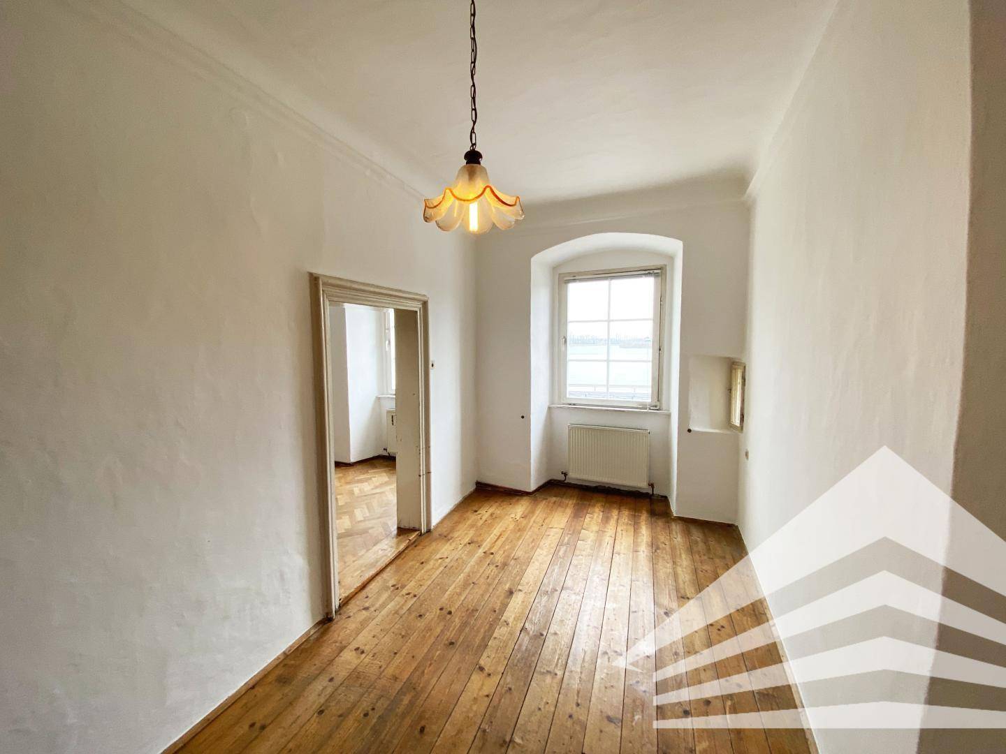 Helles Zimmer mit Holzdielenboden und einem Fenster, das viel Tageslicht hereinlässt.
