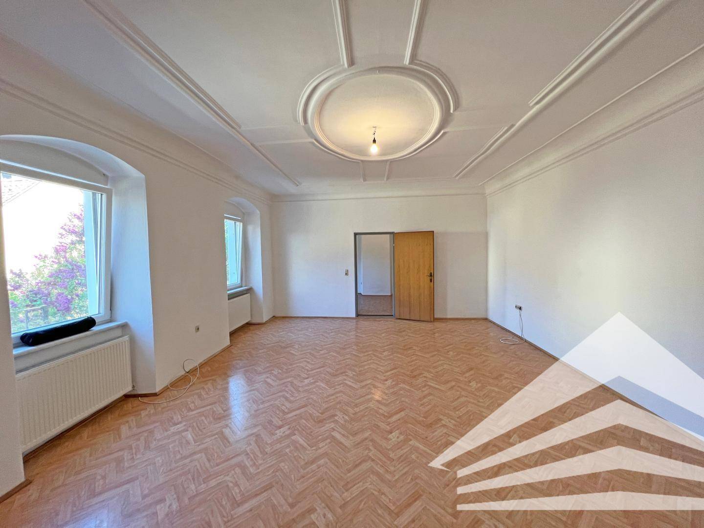 Großes Zimmer mit Stuckdecke, Parkettboden und zwei hohen Fenstern für viel Licht.