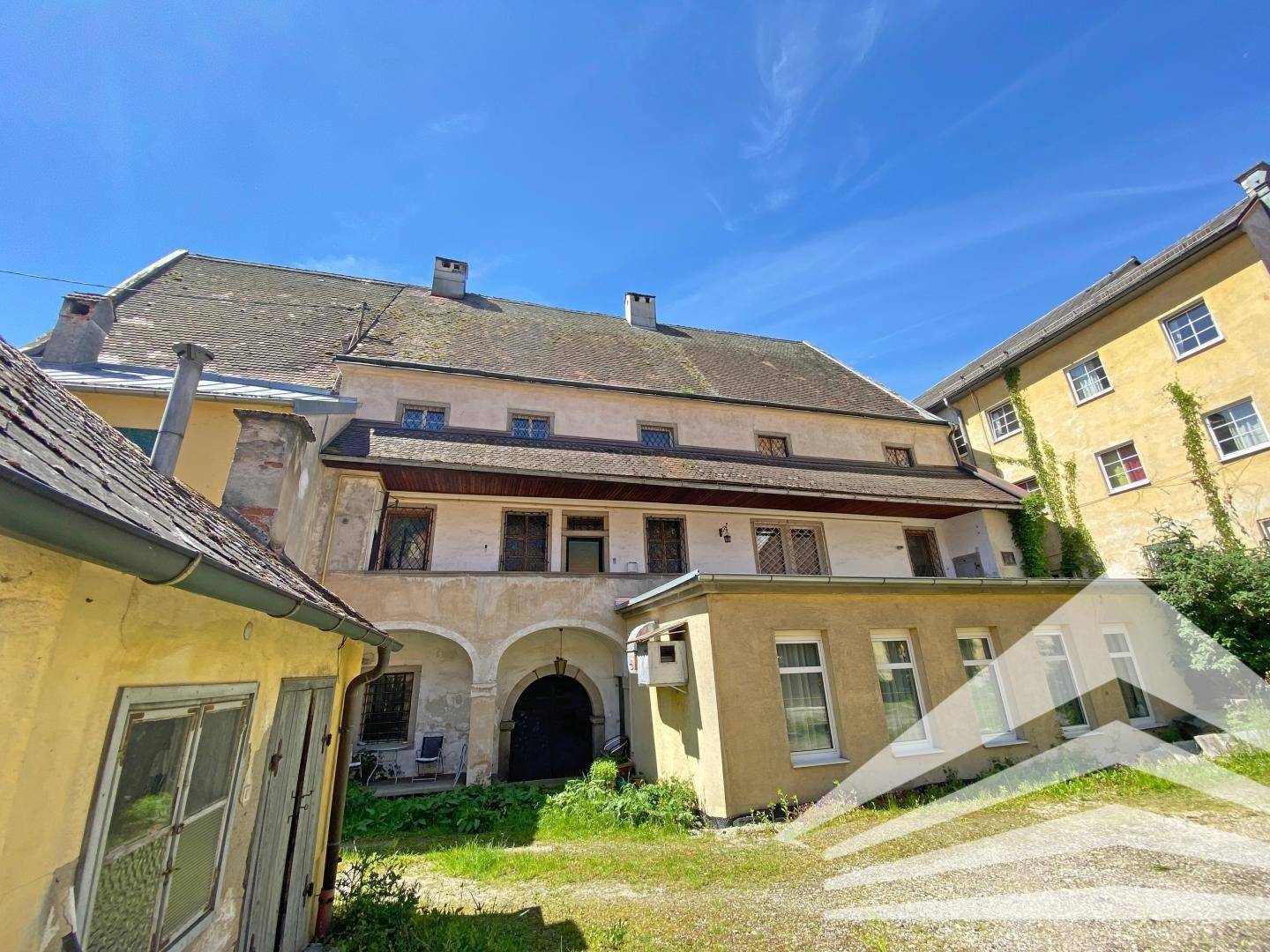 Historischer Hinterhof mit alten Gebäuden, einem Torbogen und einem unbefestigten Weg.