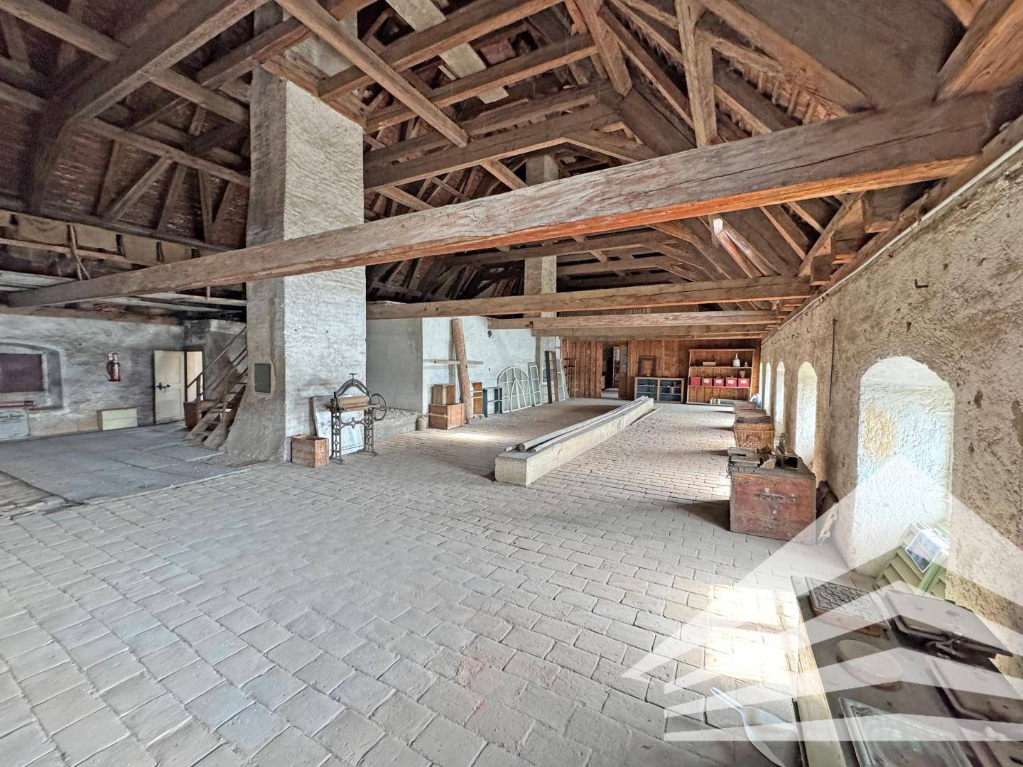 Weitläufiger Dachbodenbereich mit sichtbaren Holzbalken, Ziegelboden und viel Potenzial für Umbau.