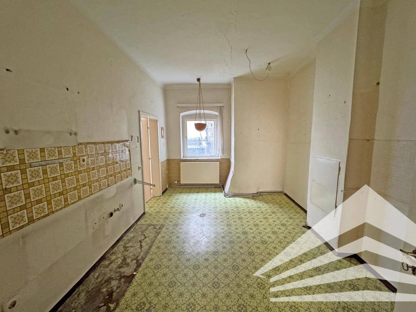 Leere Küche mit alten Fliesen an den Wänden und einem Fenster, das Licht spendet.