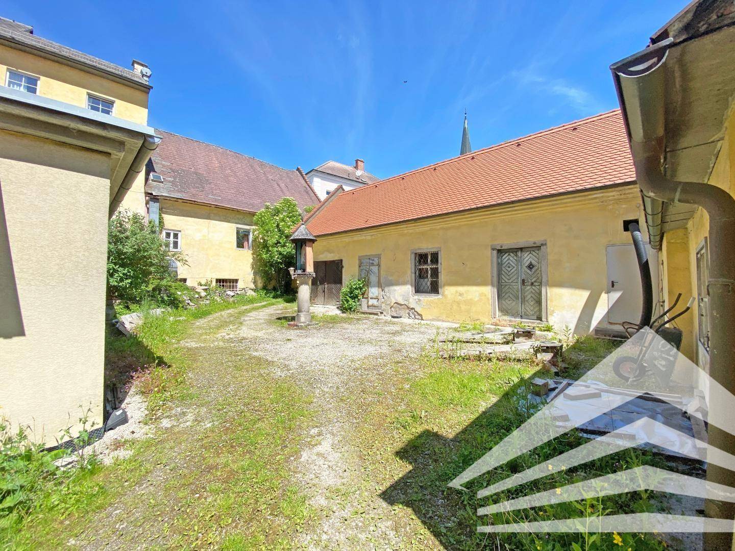 Hinterhof mit Kiesfläche, Gras und einem alten Brunnen, umgeben von historischen Gebäuden.