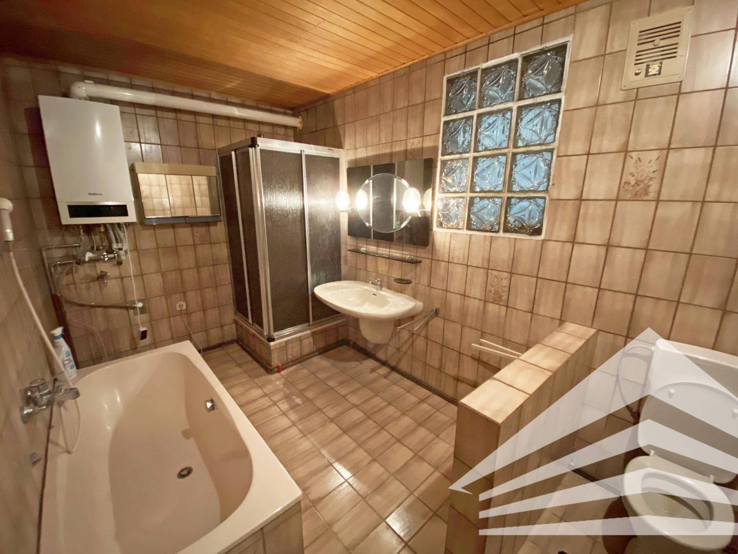 Badezimmer im Stil der 80er Jahre mit Badewanne, Dusche und braunen Fliesen.