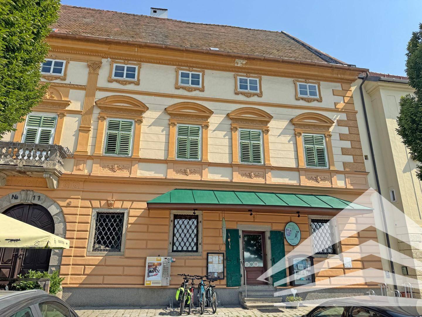 Historisches Gebäude mit oranger Fassade, grünen Fensterläden und einem kleinen Balkon über dem Eingang.