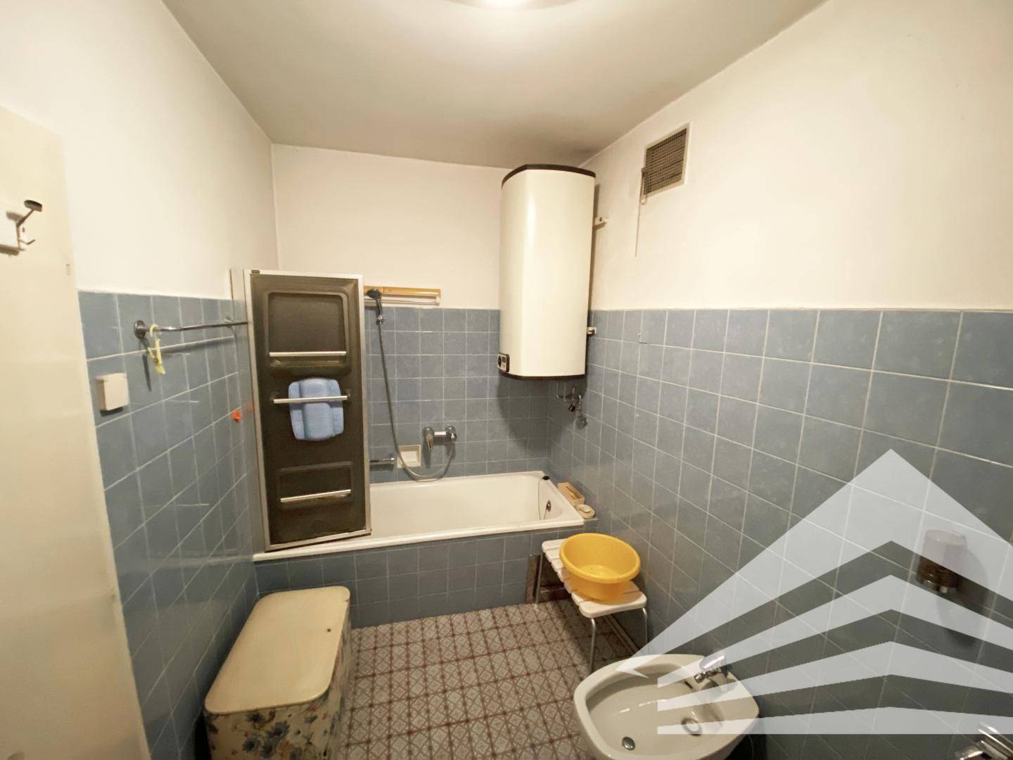 Badezimmer im Retro-Stil mit blauen Fliesen, Badewanne und Boiler an der Wand.