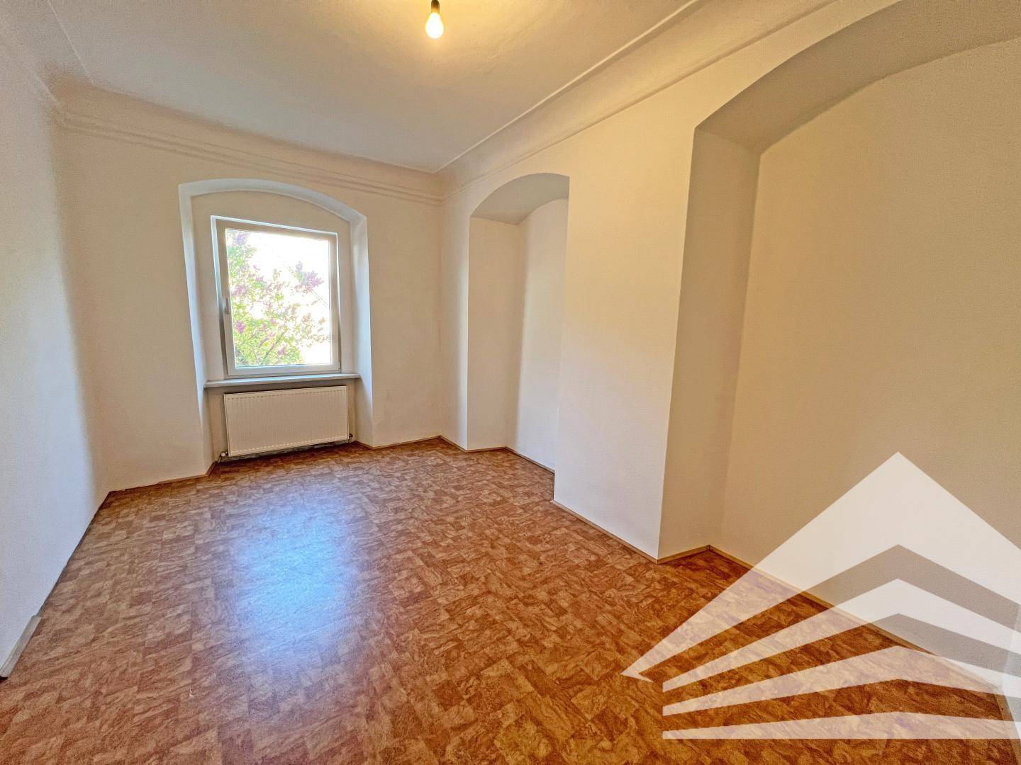 Helles Zimmer mit Parkettboden, weiß gestrichenen Wänden und einem Fenster mit Rundbogen.
