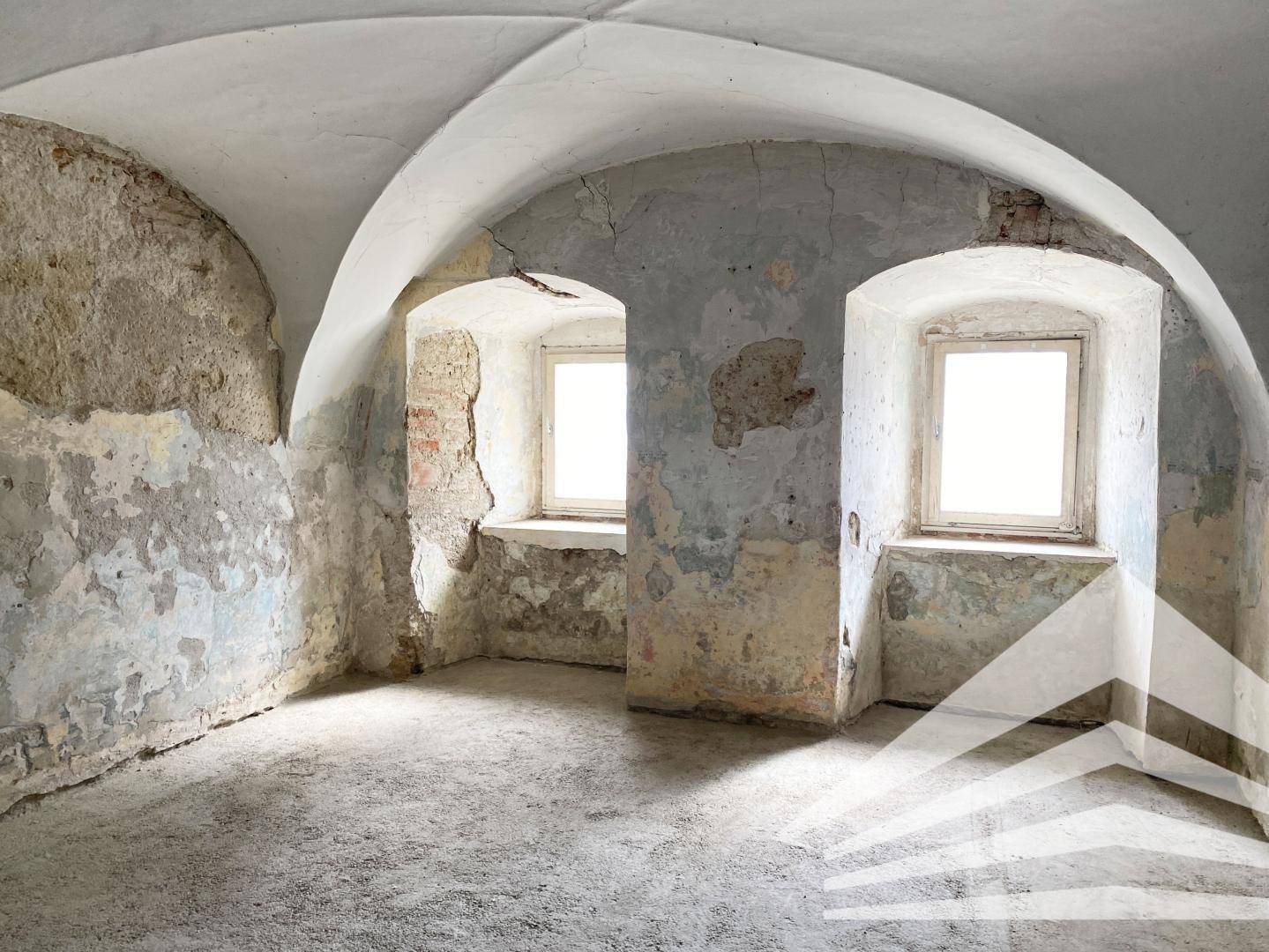 Historischer Kellerraum mit Gewölbedecke, unverputzten Wänden und zwei kleinen Fenstern.
