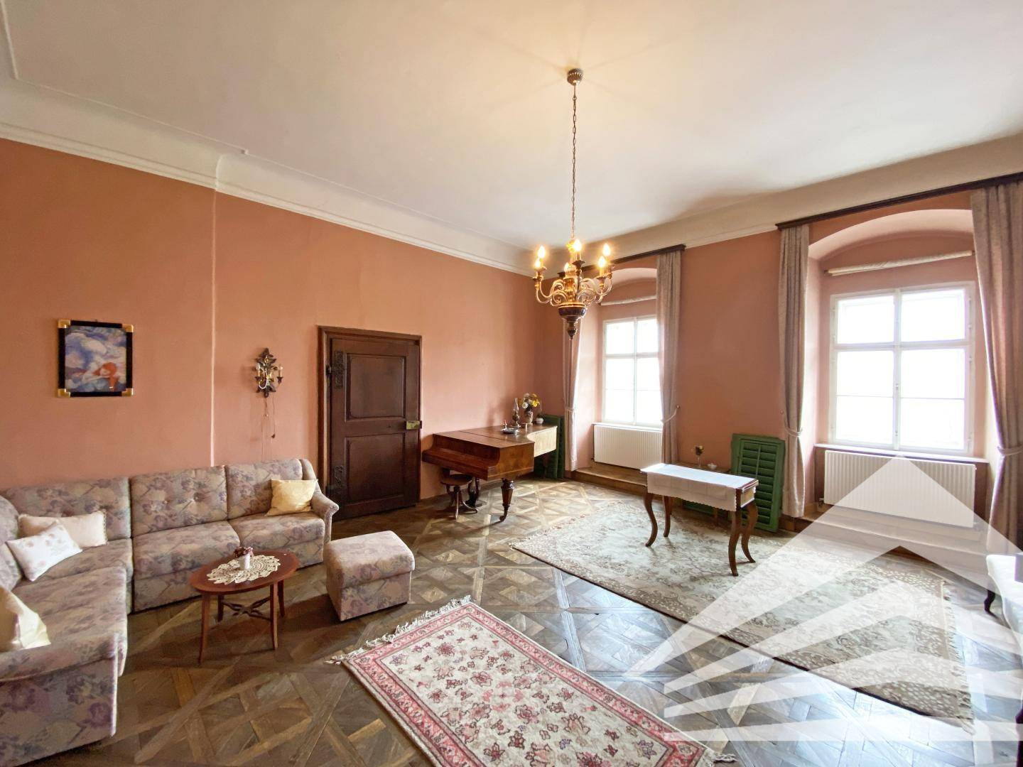 Geräumiges Wohnzimmer mit Parkettboden, Sofa und einem Kronleuchter, das viel Licht bietet.