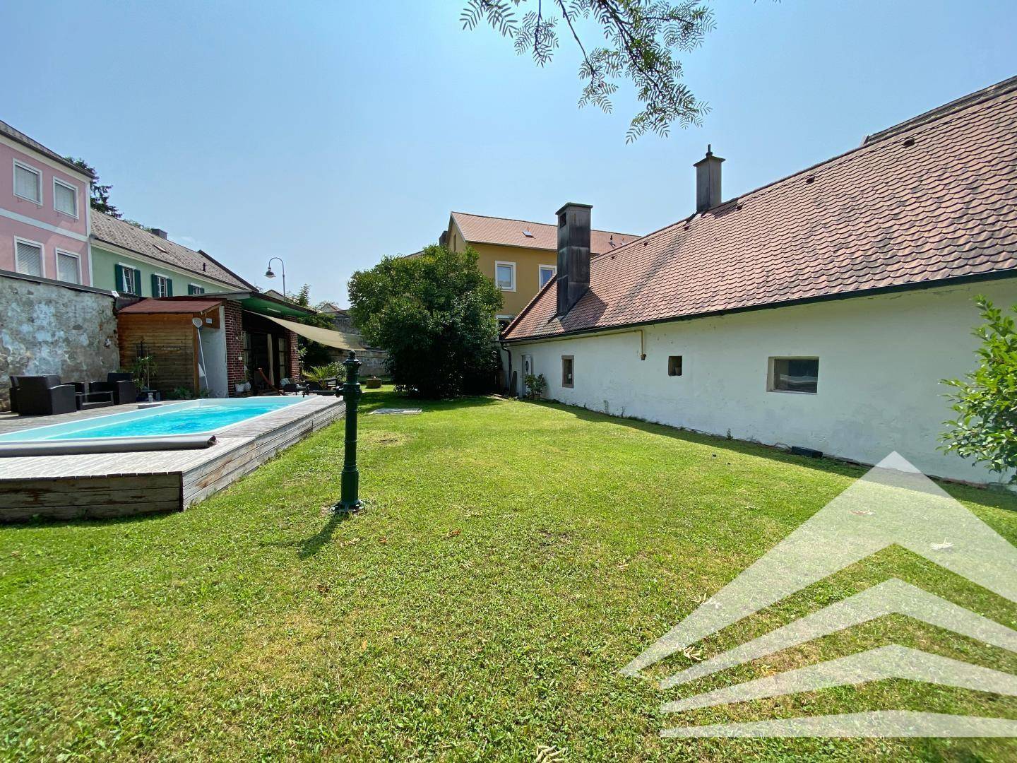 Weitläufiger Garten mit Pool und Rasenfläche, umgeben von historischen Gebäuden unter blauem Himmel.