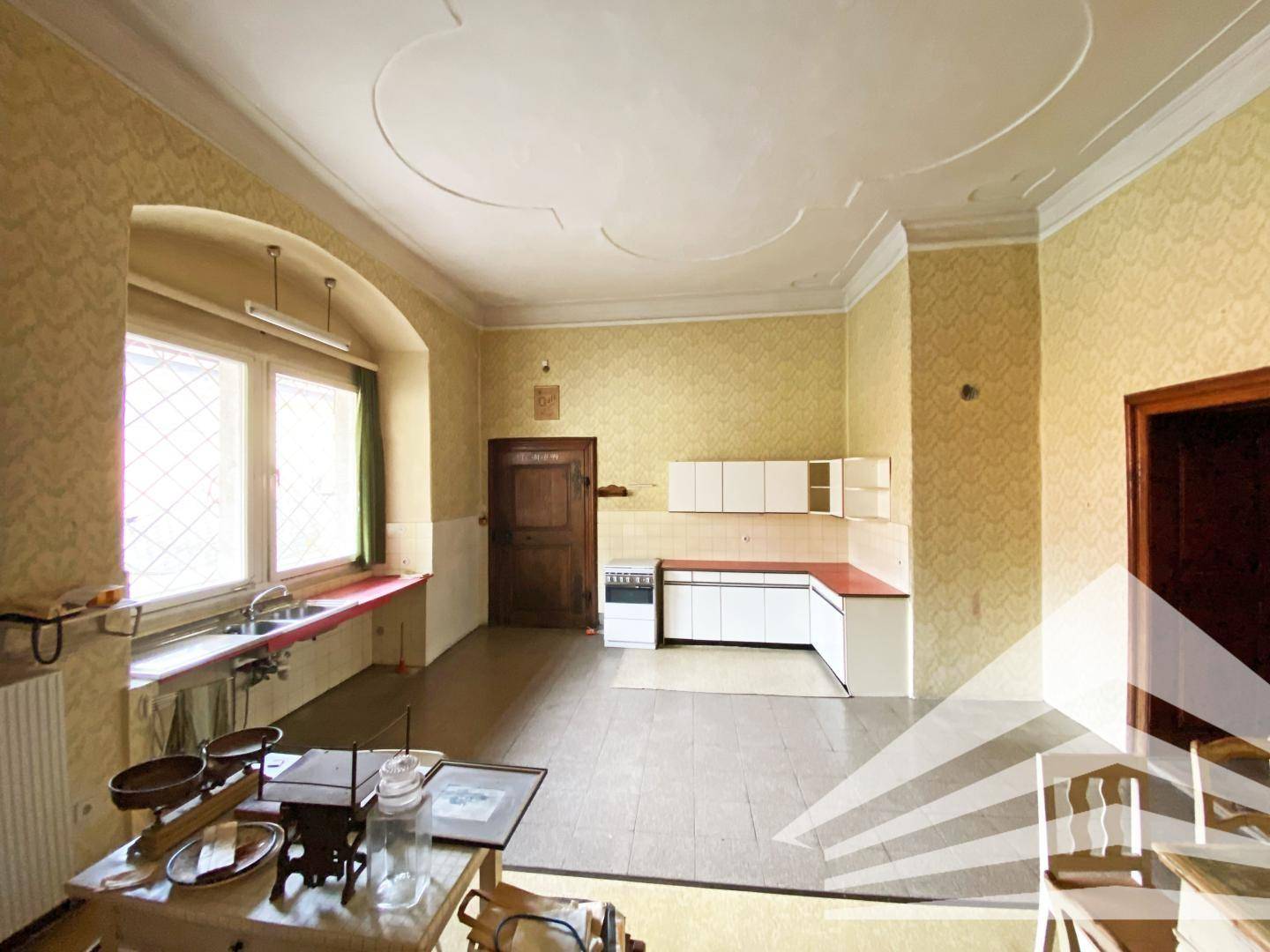 Geräumige Küche mit einfacher Einbauküche, Fliesenboden und dekorativer Stuckdecke.