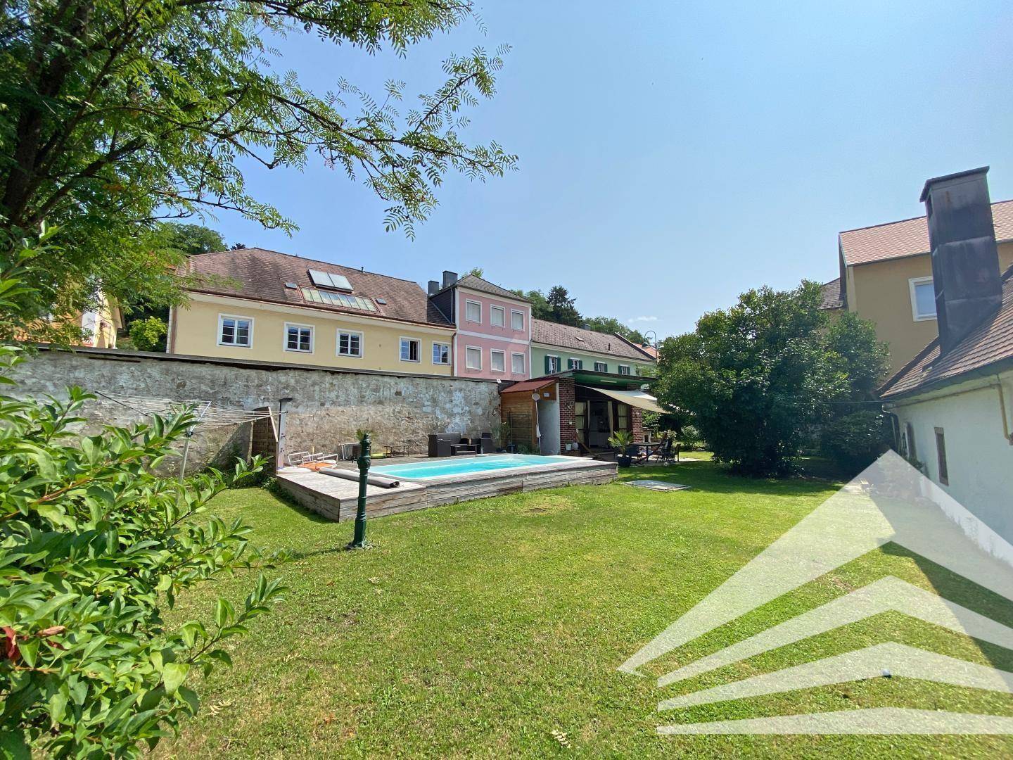 Großer Garten mit Rasenfläche, einem eingelassenen Pool und einer überdachten Terrasse im Hintergrund.