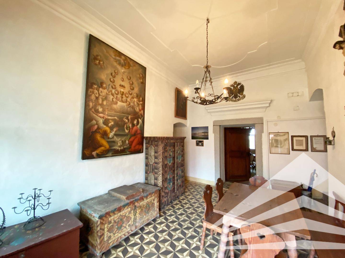 Historisches Esszimmer mit gemustertem Fliesenboden, Holztisch und antiken Möbeln.