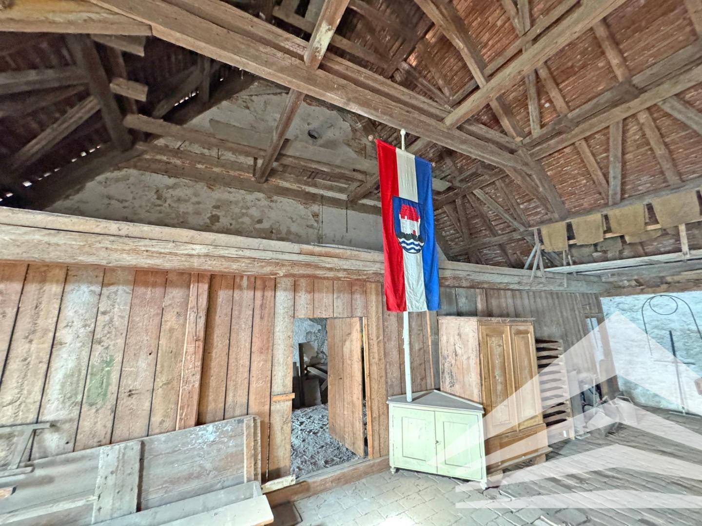 Rustikaler Dachboden mit Holzwänden, freiliegendem Dachstuhl und einer hängenden Flagge.