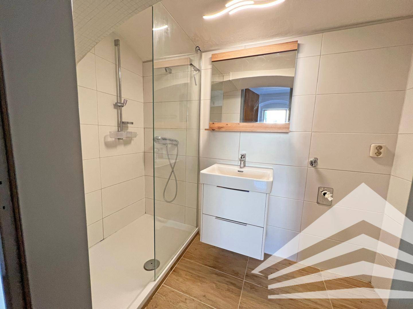 Modernisiertes Badezimmer mit begehbarer Dusche, Waschbecken und Dachschräge.