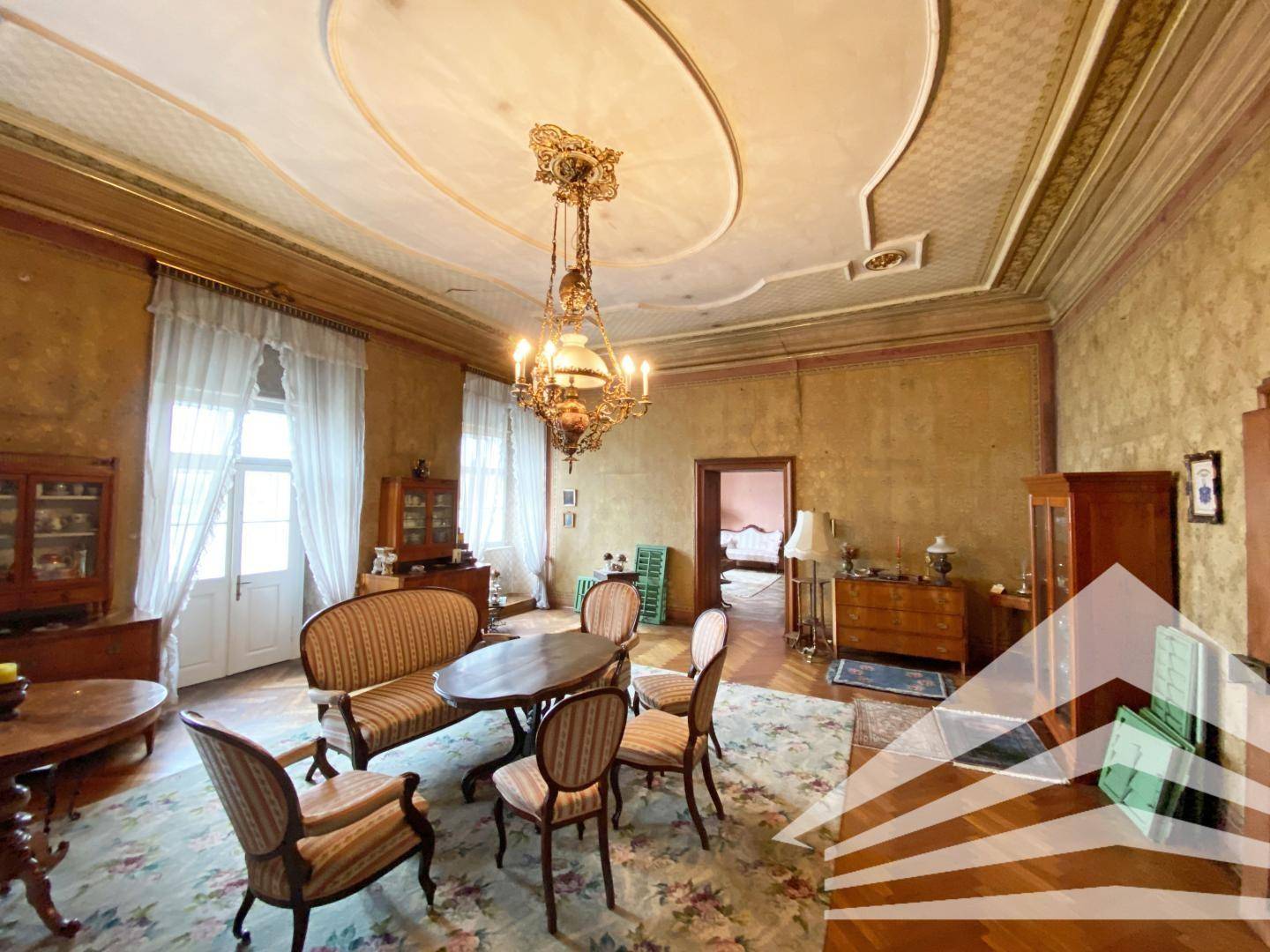 Elegantes Wohnzimmer mit Parkettboden, Stuckdecke und antiken Möbeln, das viel Licht bietet.