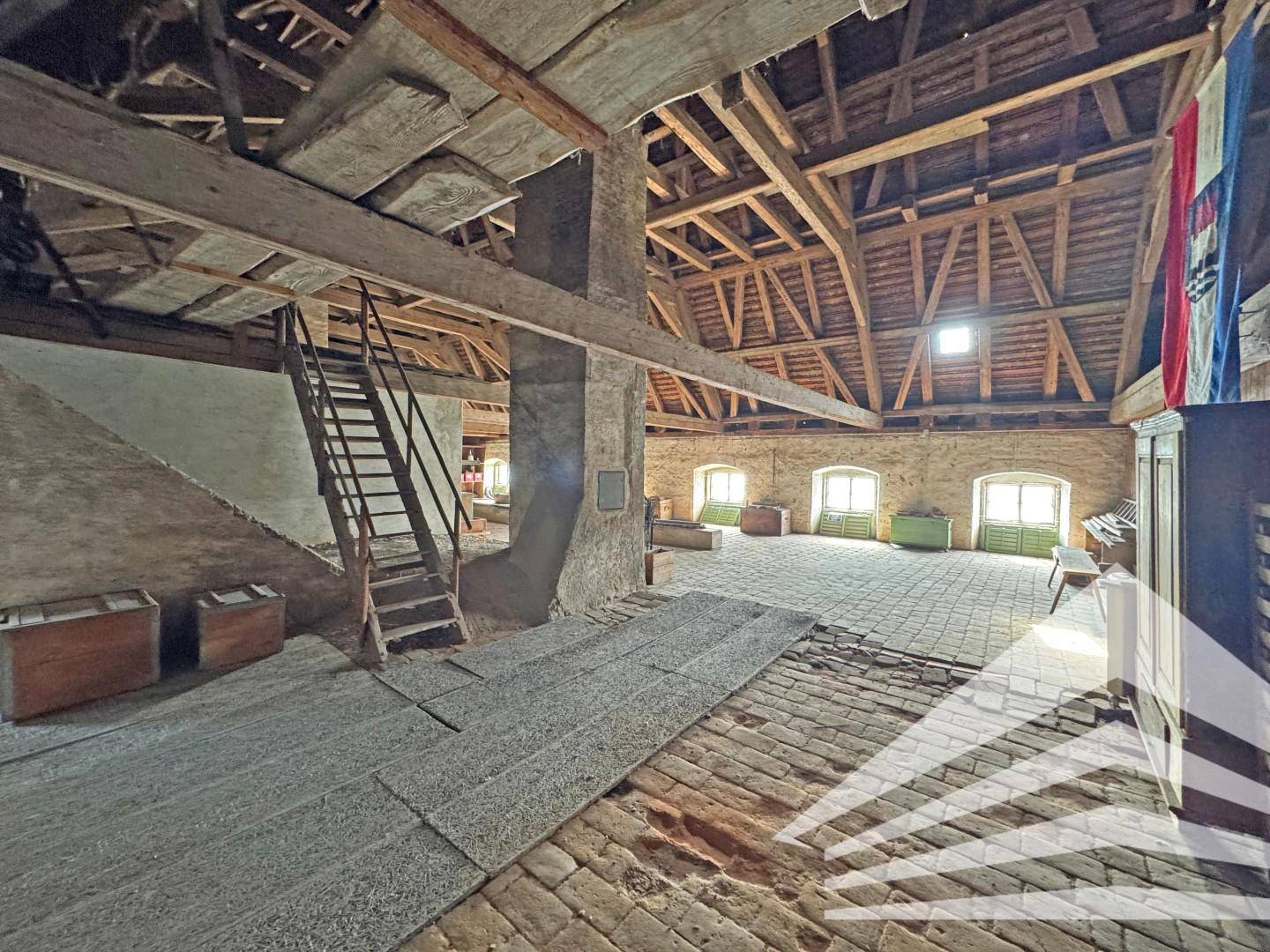 Großer Dachboden mit freiliegendem Dachstuhl, Ziegelboden und einer Metalltreppe.