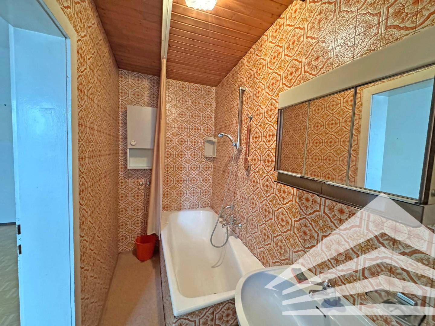 Kleines Badezimmer mit Badewanne, Waschbecken und auffälligen orangefarbenen Fliesen.