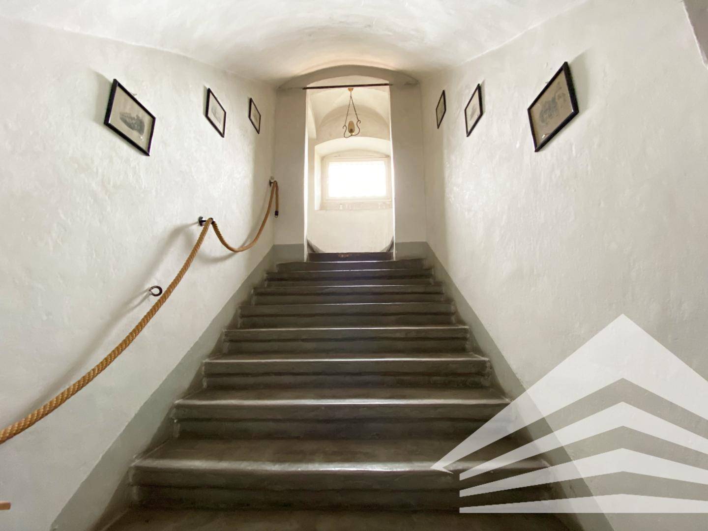 Historisches Treppenhaus mit Steinstufen und einem Seilgeländer, das nach oben führt.