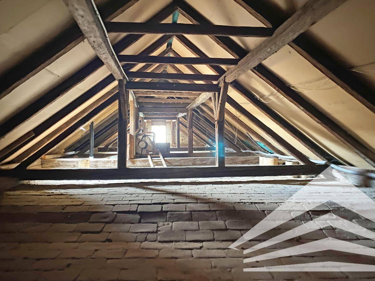 Dachboden mit freiliegenden Holzbalken und Ziegelboden, bereit für einen möglichen Ausbau.