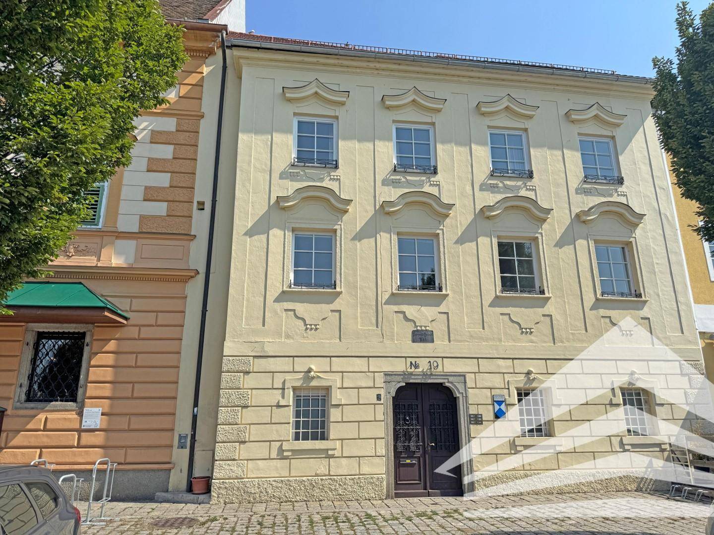 Klassisches Gebäude mit heller Fassade, verzierten Fenstern und einem traditionellen Eingangsbereich.