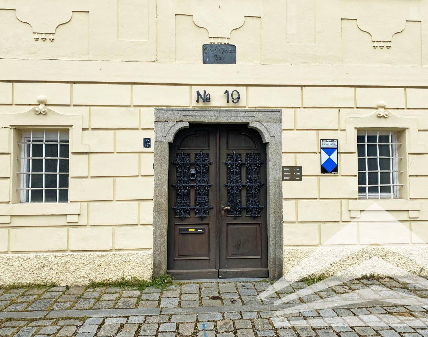 Eingangsbereich eines historischen Gebäudes mit verzierten Holztüren und schmiedeeisernen Gittern.