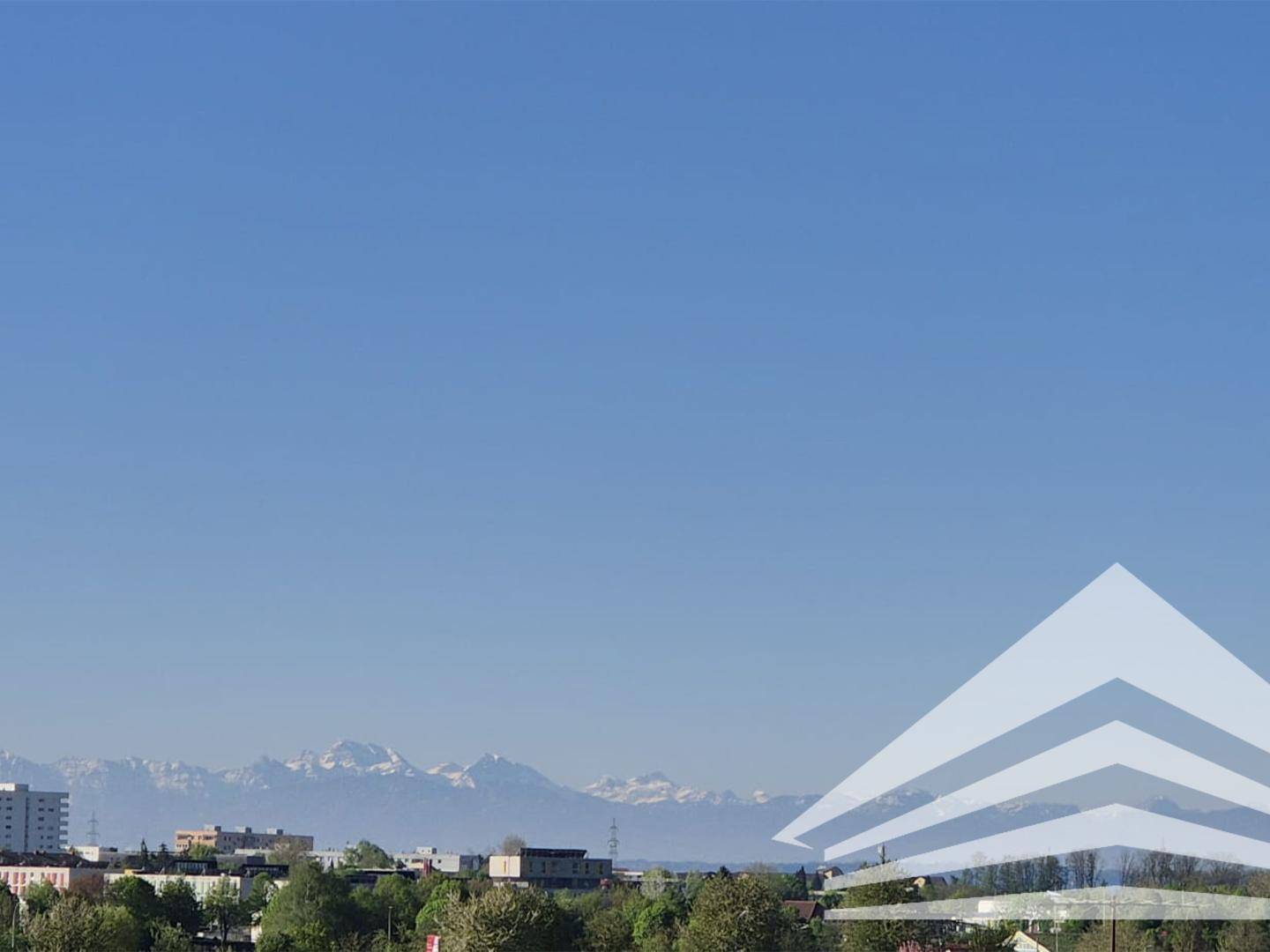 Panoramablick auf schneebedeckte Berge über einer städtischen Landschaft unter klarem Himmel.