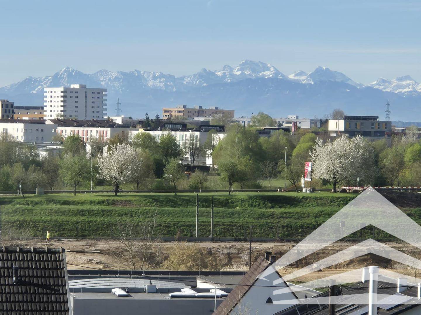 Panoramablick über eine Stadt mit grünen Flächen und schneebedeckten Bergen im Hintergrund.