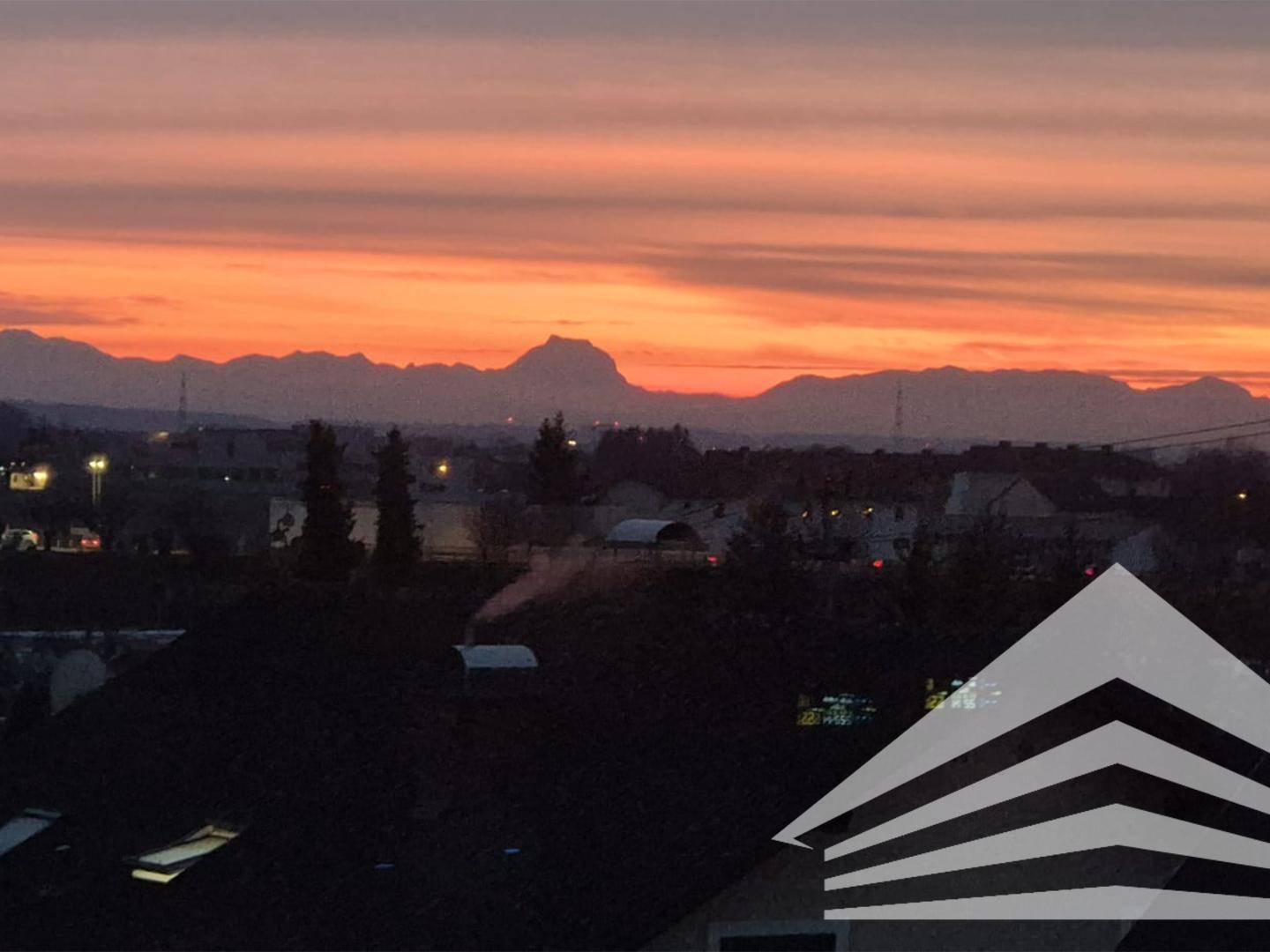 Malerischer Sonnenuntergang über einer Stadt mit Bergen am Horizont und einem leuchtenden Himmel.