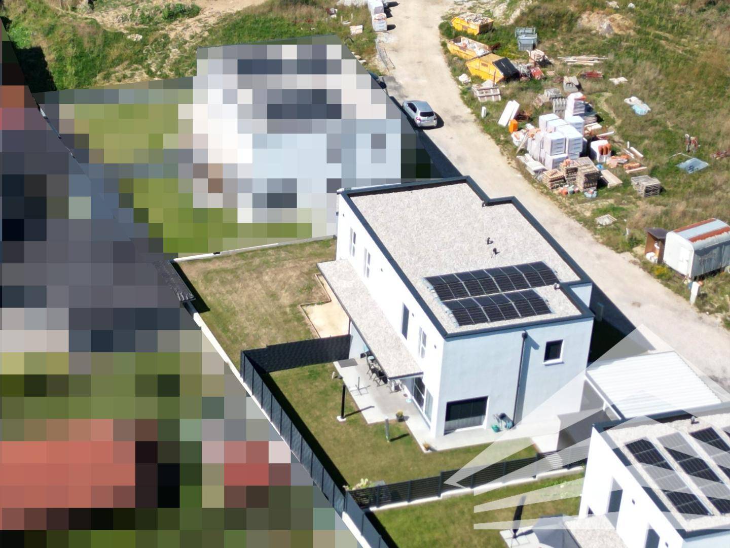 Luftaufnahme eines modernen Hauses mit Flachdach und Photovoltaikanlage, umgeben von Grünflächen und Baustellen.