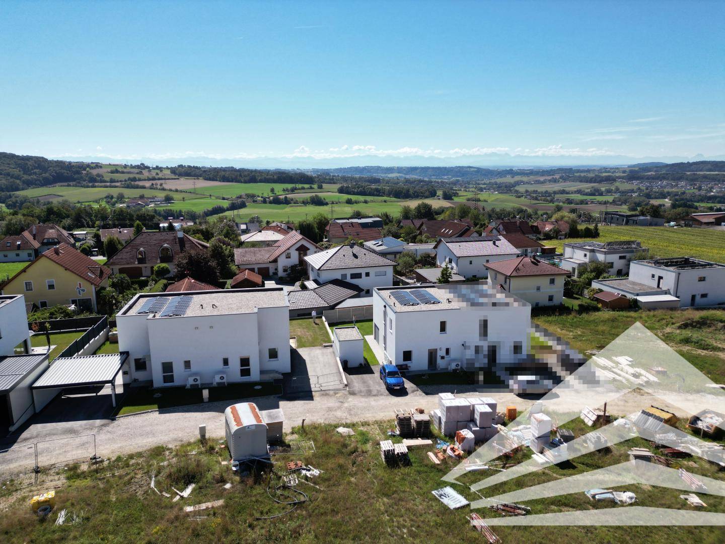 Luftaufnahme einer neuen Wohnsiedlung mit modernen Häusern und Photovoltaikanlagen, umgeben von grüner Landschaft.
