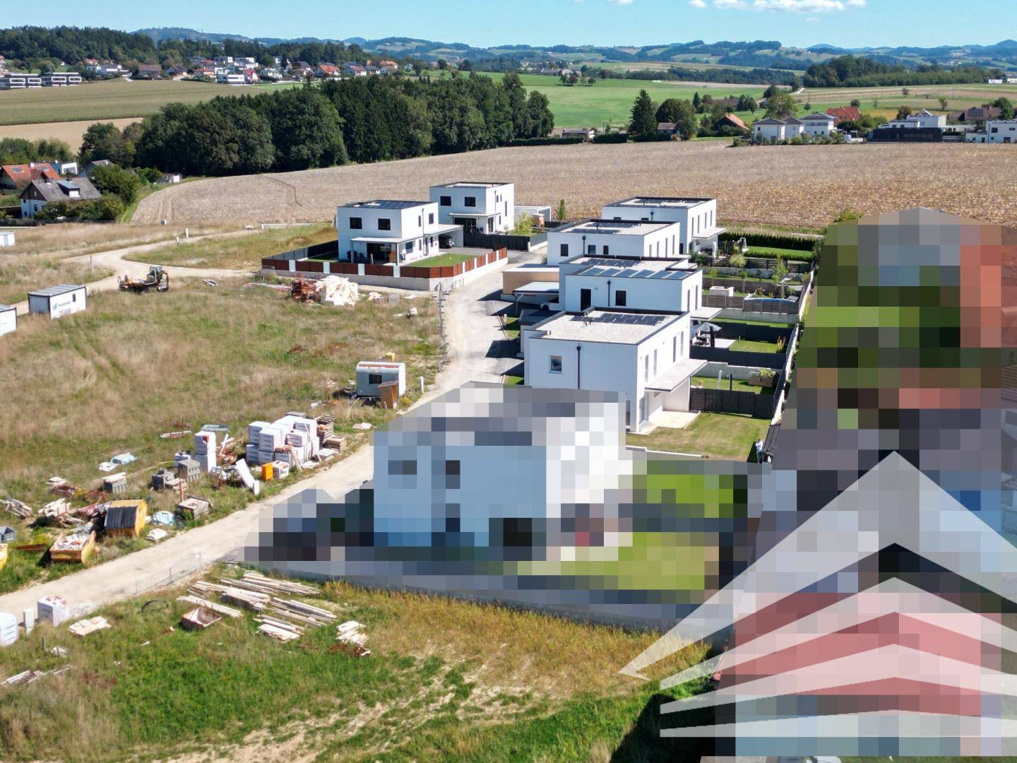Luftaufnahme einer Siedlung moderner Häuser in ländlicher Umgebung mit weiten Feldern und Hügeln.