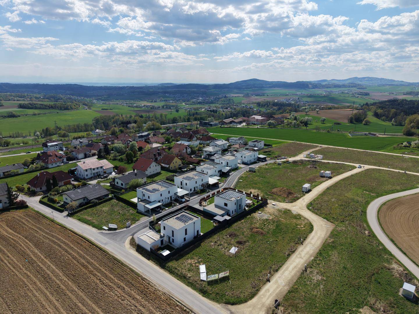 Weitläufige Luftansicht einer Neubausiedlung, umgeben von grünen Feldern und ländlicher Landschaft.