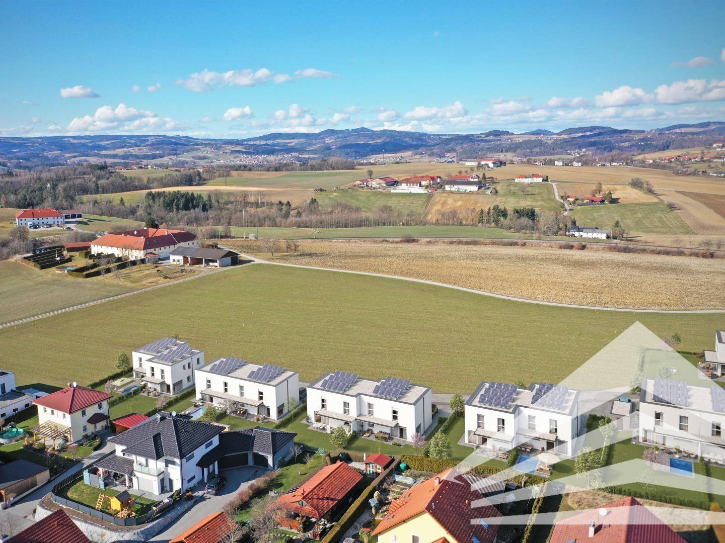 Luftaufnahme einer Wohnsiedlung mit modernen Häusern und weitem Blick auf die hügelige Landschaft.
