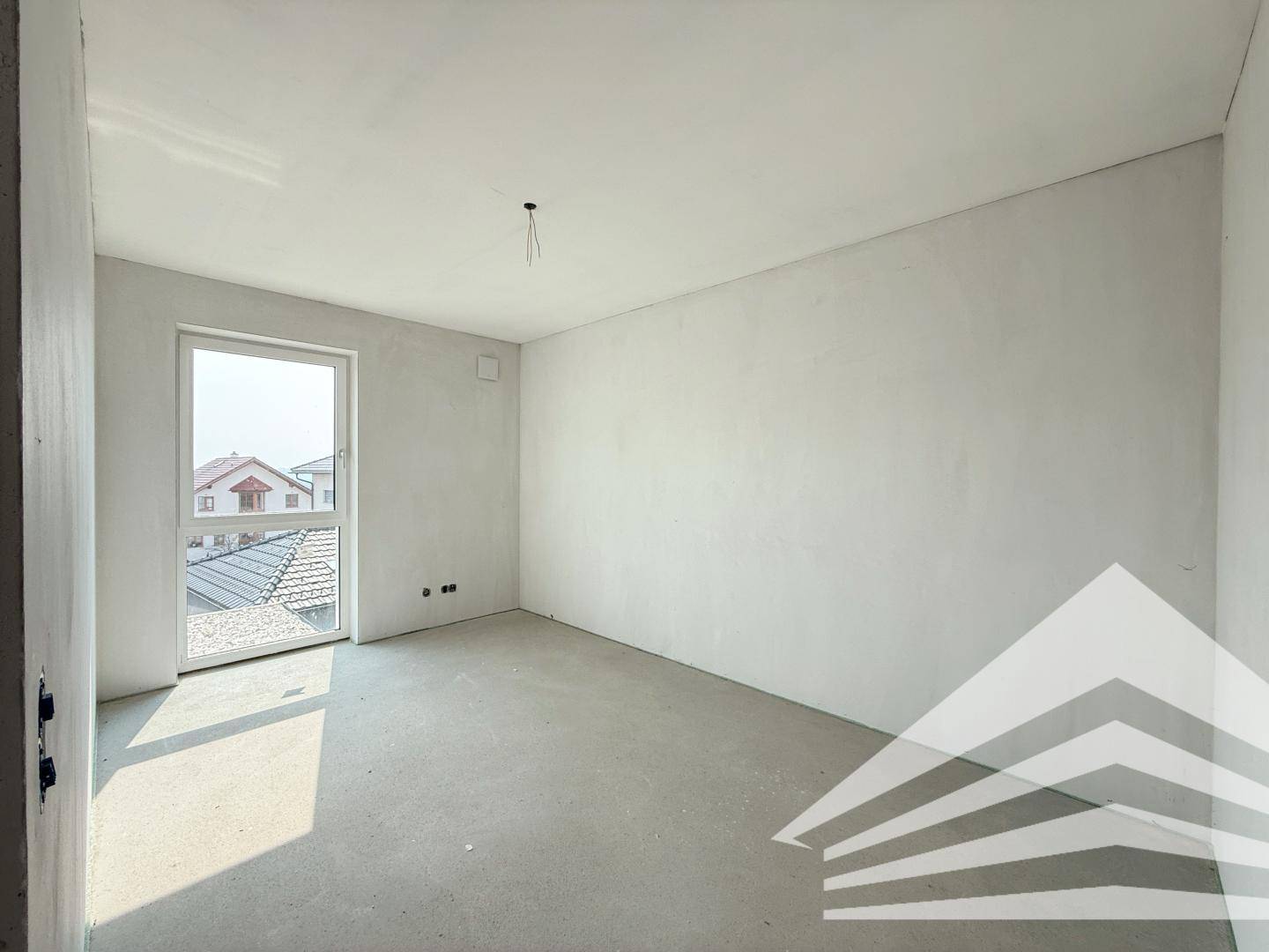Unfertiges Zimmer mit weiß gestrichenen Wänden und Fenster mit Blick auf die Dächer.