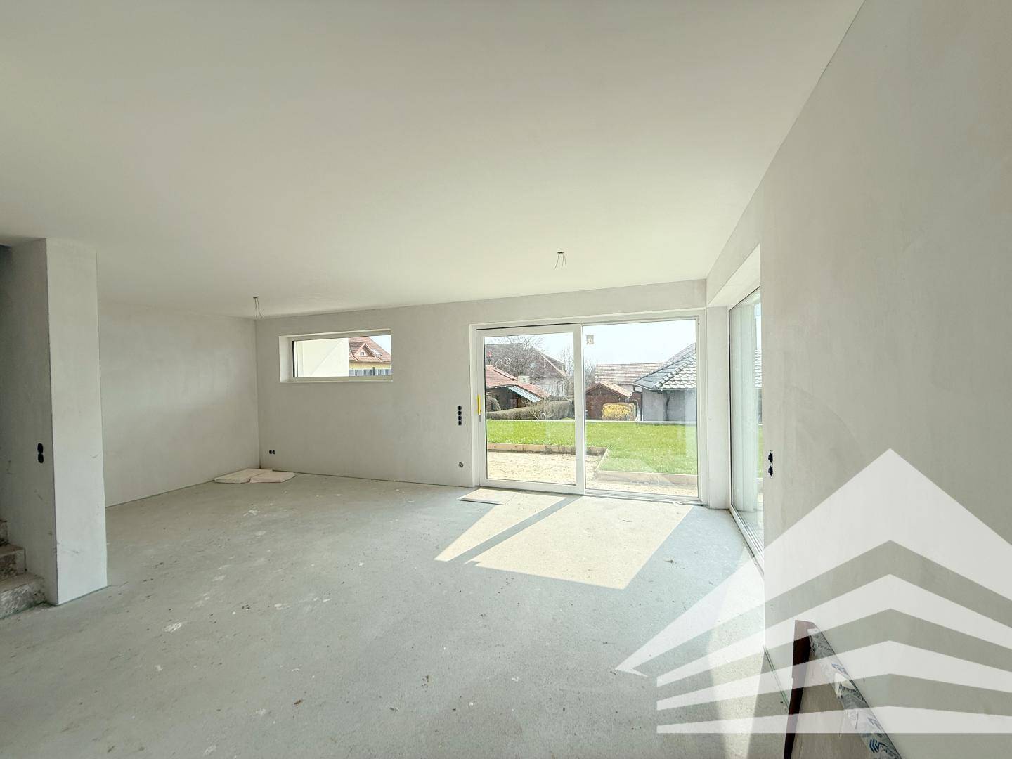Geräumiger, unfertiger Wohnbereich mit Schiebetür zum Garten und viel Tageslicht.