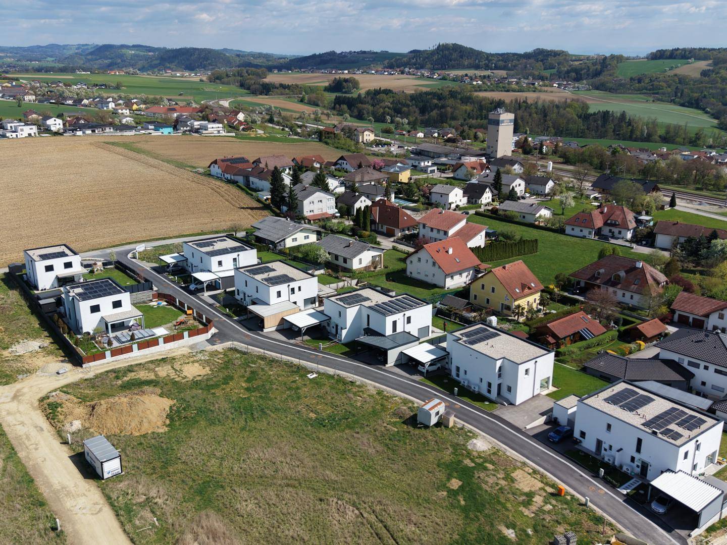 Luftaufnahme einer modernen Wohnsiedlung mit Neubauten inmitten grüner Landschaft.