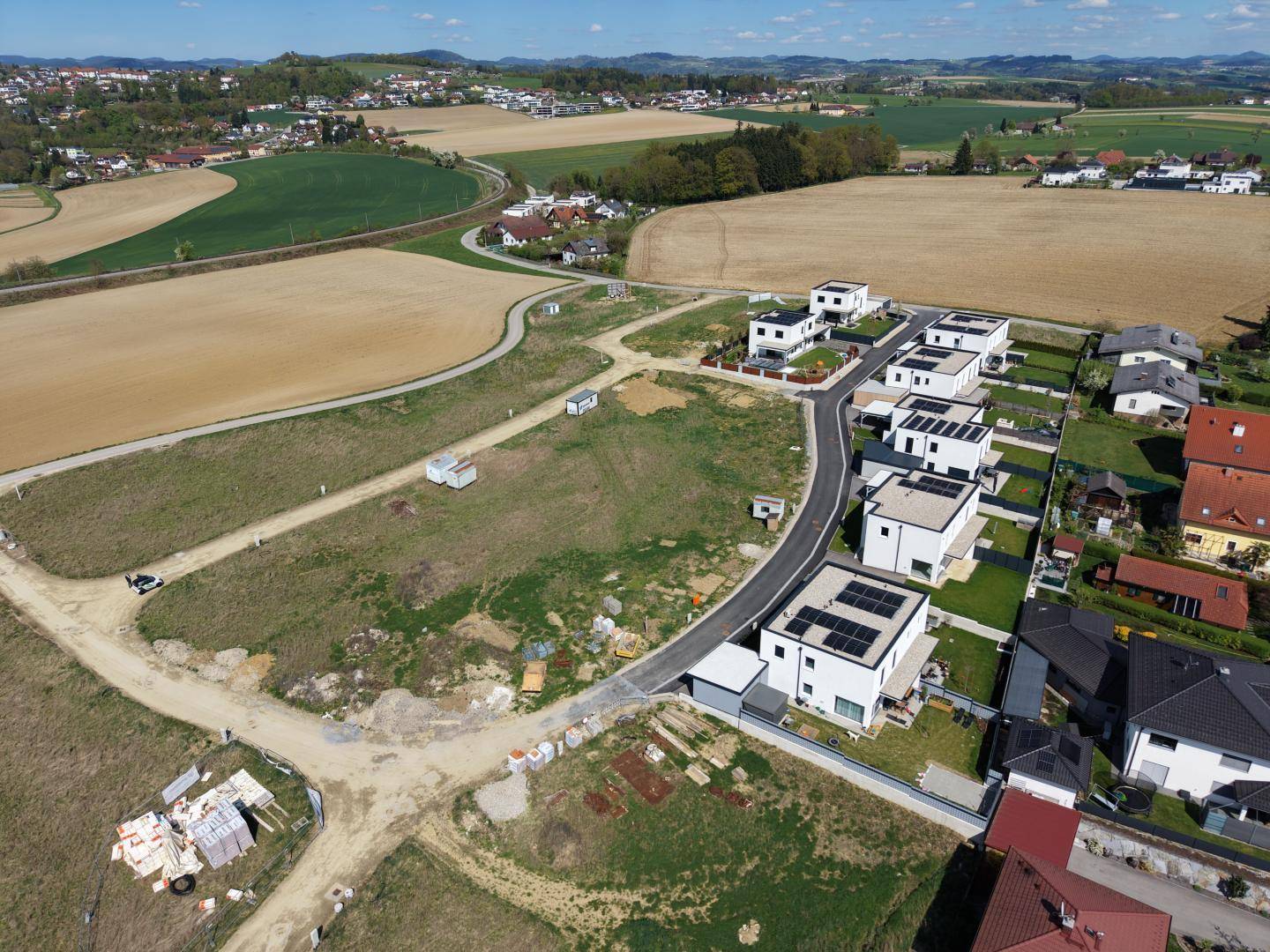 Weitläufige Luftaufnahme einer neuen Wohnsiedlung mit unbebauten Grundstücken und Feldern.
