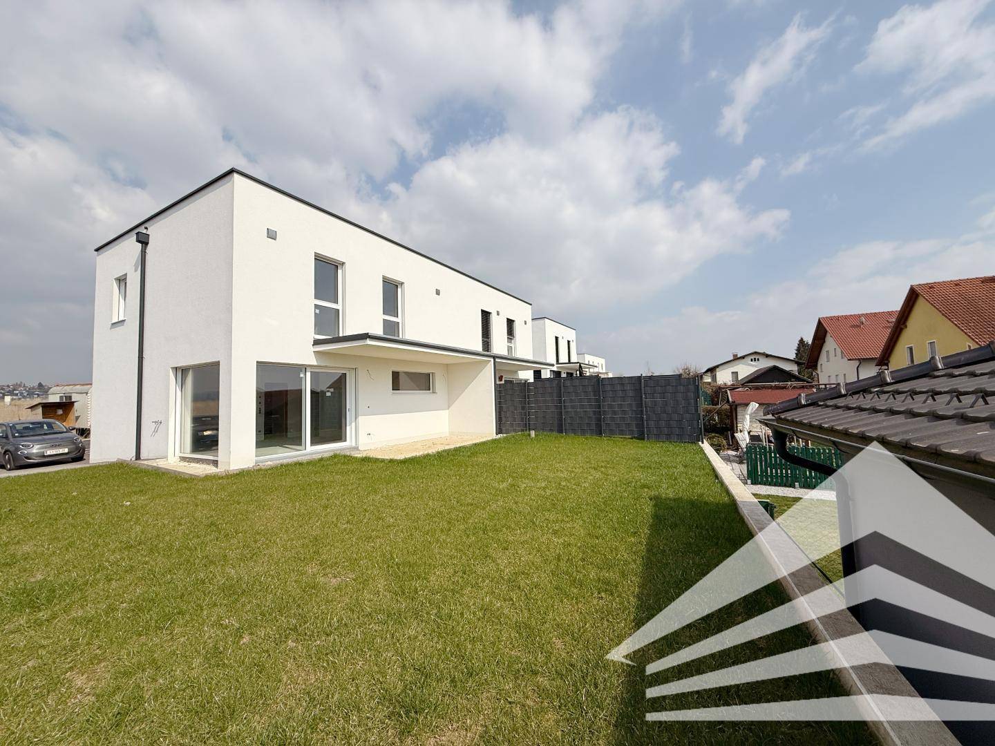 Moderne Hausfassade mit großem Rasenbereich und Blick auf die Nachbarschaft.